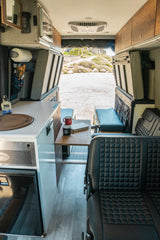 Inside a spacious rv rental camper van, with a compact kitchen, dining area, comfy seats, and a wide view of nature from the rear.