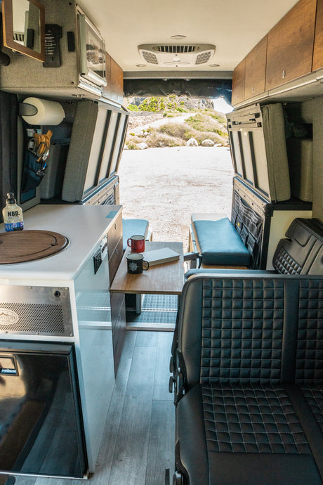 Inside a spacious rv rental camper van, with a compact kitchen, dining area, comfy seats, and a wide view of nature from the rear.
