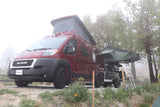 Red pop-top camper van, an RV rental, with an attached rooftop tent, parked in a foggy outdoor setting.