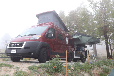 Red pop-top camper van, an RV rental, with an attached rooftop tent, parked in a foggy outdoor setting.