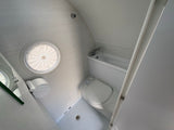 Bright RV rental bathroom with white curved walls, featuring a toilet, compact tub/shower, and round ceiling vent.