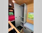 An rv rental interior featuring a red bed, kitchen, wood ceiling, gray storage cabinet, and comfy bench seating.