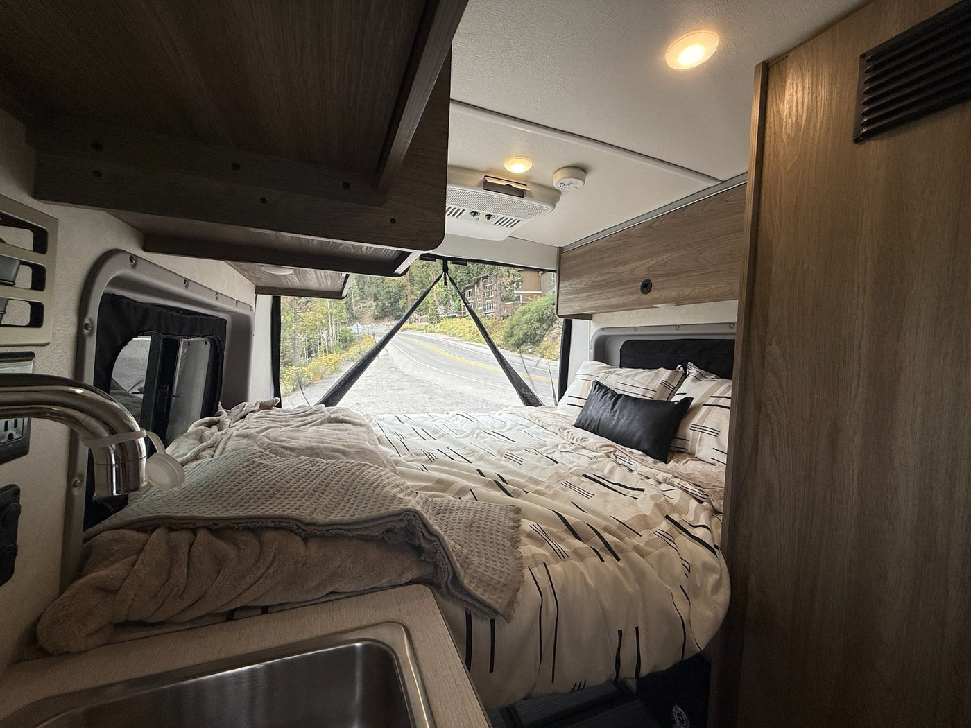  and a scenic view through rear windows.|A silver Winnebago Ram ProMaster camper van RV rental drives on a scenic road with trees — photo 13