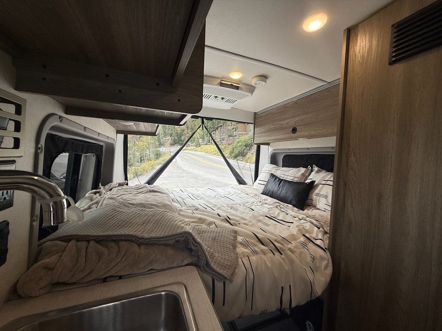 Cozy rv rental interior features a bed, small sink, and a scenic road view for your journey.