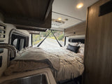 Cozy rv rental interior features a bed, small sink, and a scenic road view for your journey.