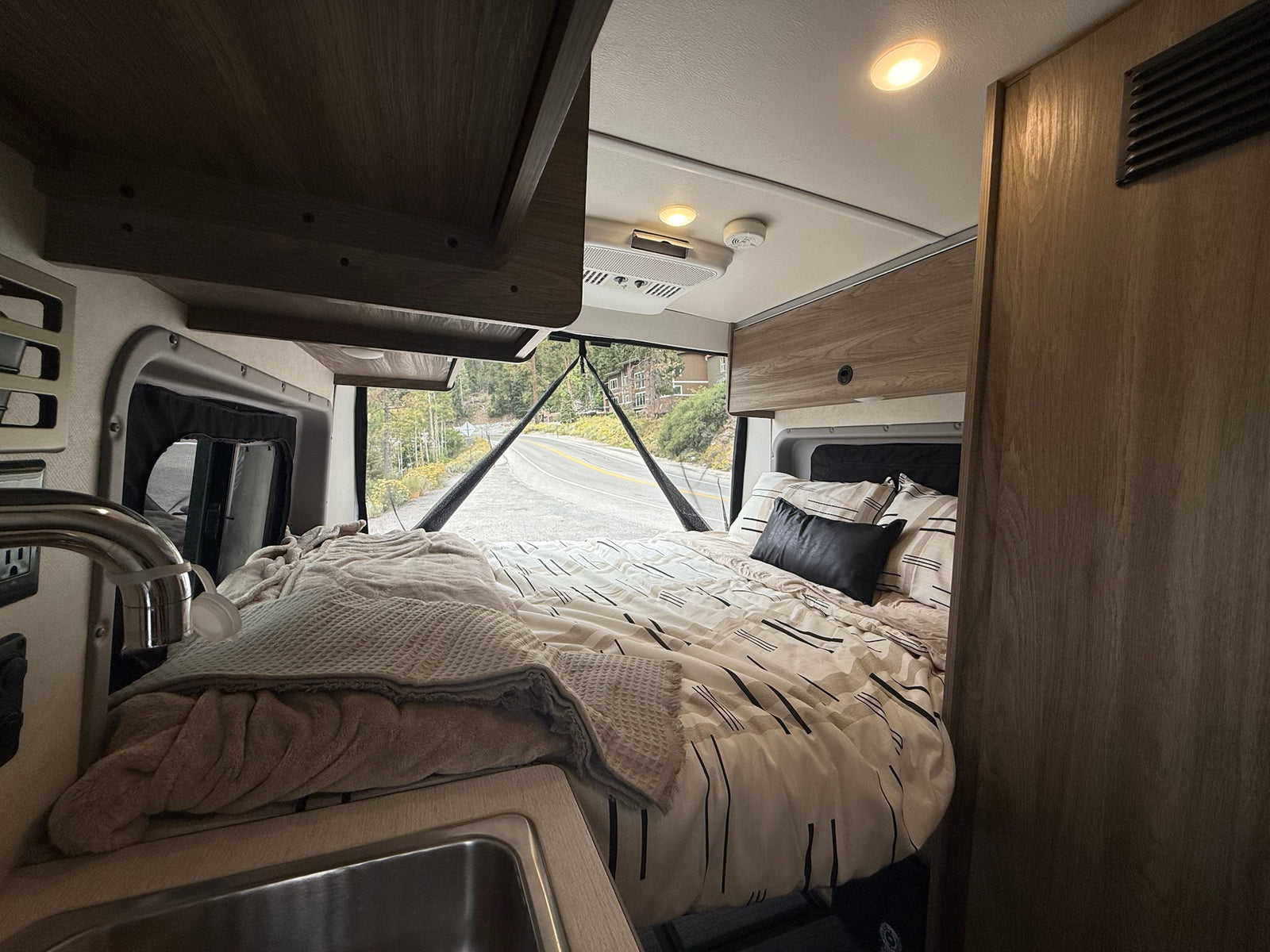 Cozy rv rental interior features a bed, small sink, and a scenic road view for your journey.