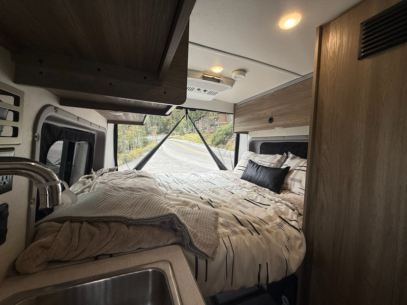  and a scenic view through rear windows.|A silver Winnebago Ram ProMaster camper van RV rental drives on a scenic road with trees — photo 13