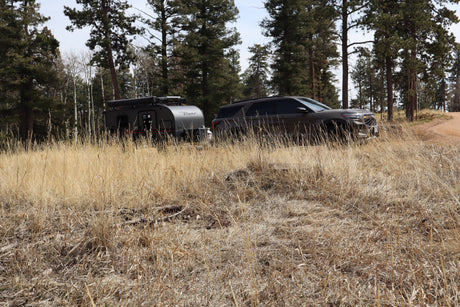 SUV towing InTech Flyer camper for an rv rental adventure in a pine forest with dry grass.