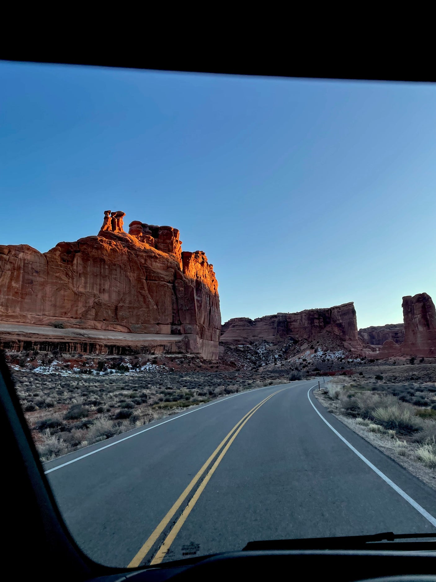 RV rental driving through a red rock desert. Towering, sunlit formations line a winding road. A clear view from inside the vehicle.