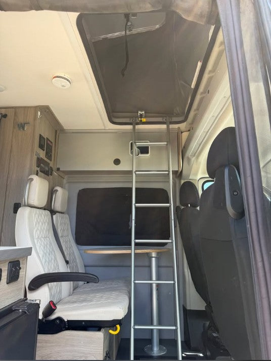 RV rental camper van interior. Ladder to upper bed, with white quilted seats and a small table below. — photo 9