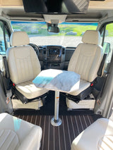 Inside an rv rental: Two cream captain's chairs face a table, creating a cozy dining area. Dark wood floor and TV visible.