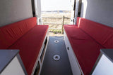 Step into this RV rental! Two red benches, textured walls, and a patterned floor lead to an open rear view of a field & lake.