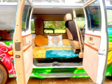 Colorful rv rental camper van interior: open doors reveal a cozy bed with vibrant pillows, ready for adventure.