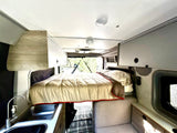 Cozy rv rental interior featuring a comfortable bed, kitchenette, and overhead storage. Ideal camper van living space.