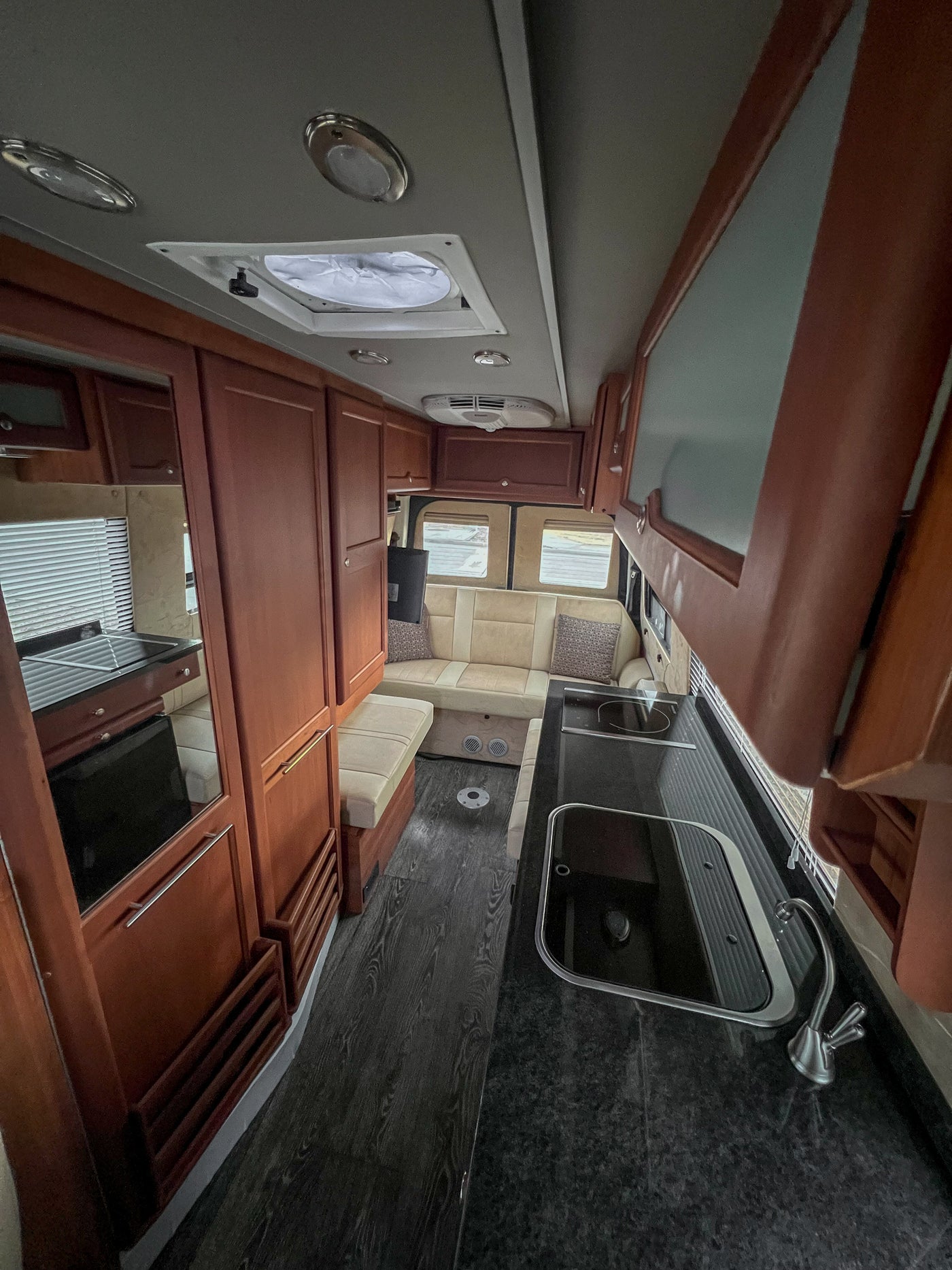 RV rental interior: galley kitchen with sink/stove, cream seating, and wood cabinets for comfortable travel. — photo 10