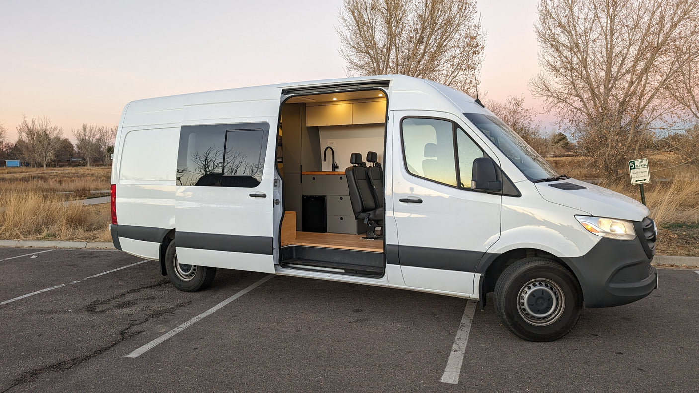 This white camper van RV rental is parked with its side door open, showcasing a modern interior kitchen.