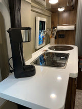 An RV rental's modern kitchen area with white countertops, integrated sink and stovetop, and a coffee maker.