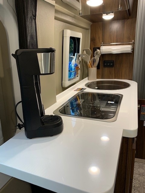 An RV rental's modern kitchen area with white countertops, integrated sink and stovetop, and a coffee maker. — photo 3