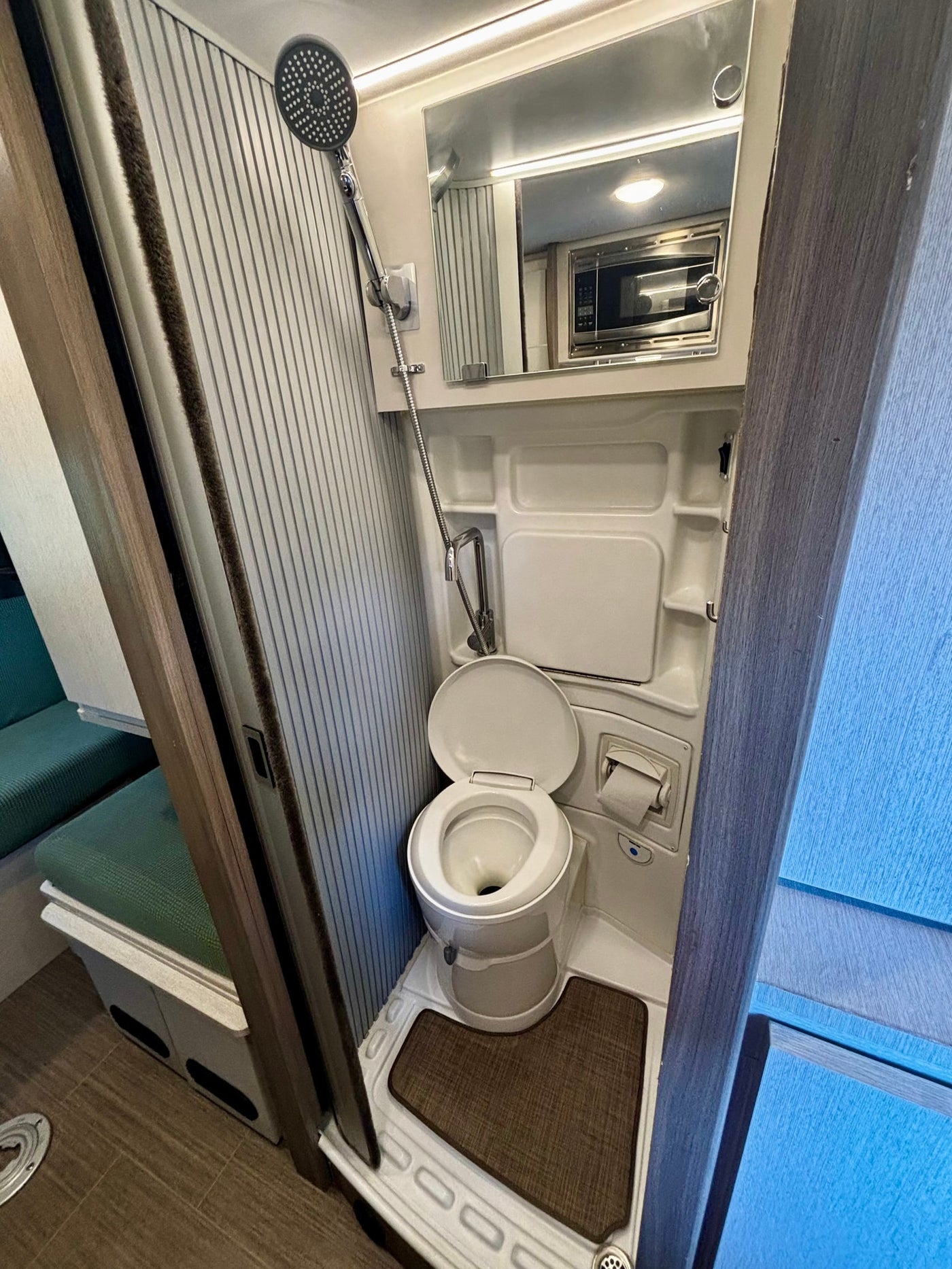 This RV rental's compact bathroom features a toilet, shower, and a mirror reflecting a microwave. Efficient design for travel. — photo 11
