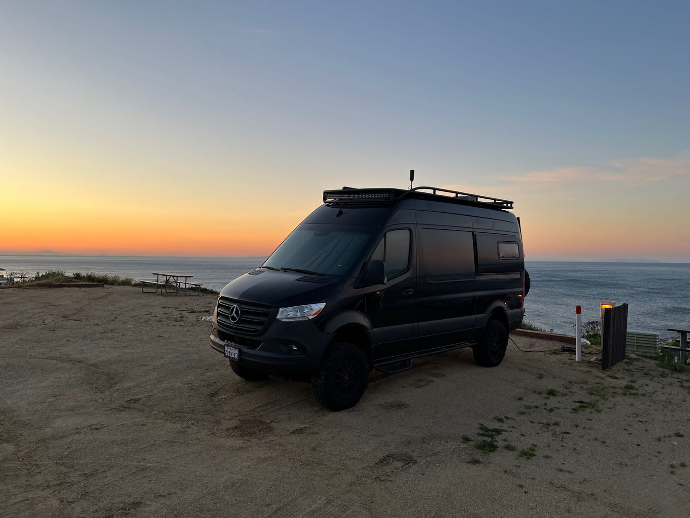Black Mercedes-Benz Sprinter RV rental at sunset by the ocean. Ideal camper van for your next adventure or road trip. — photo 18