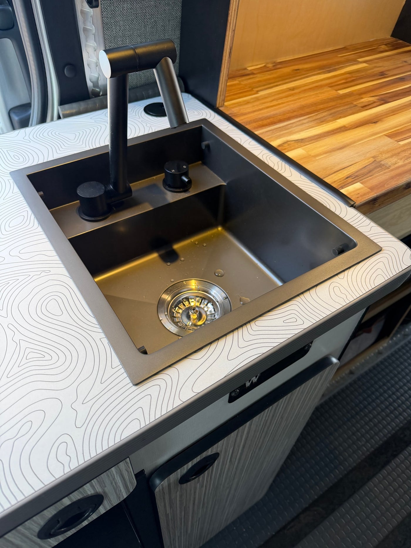 Modern black sink & faucet in a stylish RV rental kitchen with a unique topographic map countertop & wood accents. — photo 11