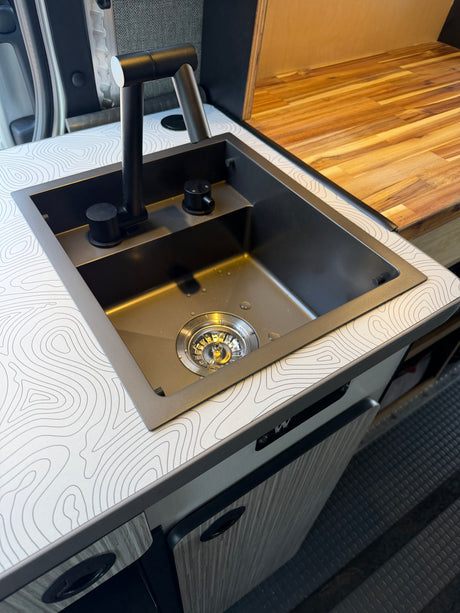 Modern black sink & faucet in a stylish RV rental kitchen with a unique topographic map countertop & wood accents.