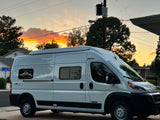 White Winnebago Solis, a camper van suitable for an RV rental, parked on a street at sunset with vibrant orange clouds.