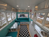 Retro teal diner-style RV rental interior with checkered rug, metal cabinets, and cozy booth seating.