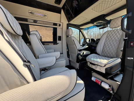 Luxury RV rental interior: white quilted leather seating, a screen, and a visible fire extinguisher for safety. Spacious & comfortable.