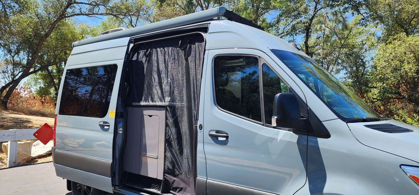 Light blue camper van RV rental with an open side door, revealing a functional sink and protective screen for outdoor adventures.