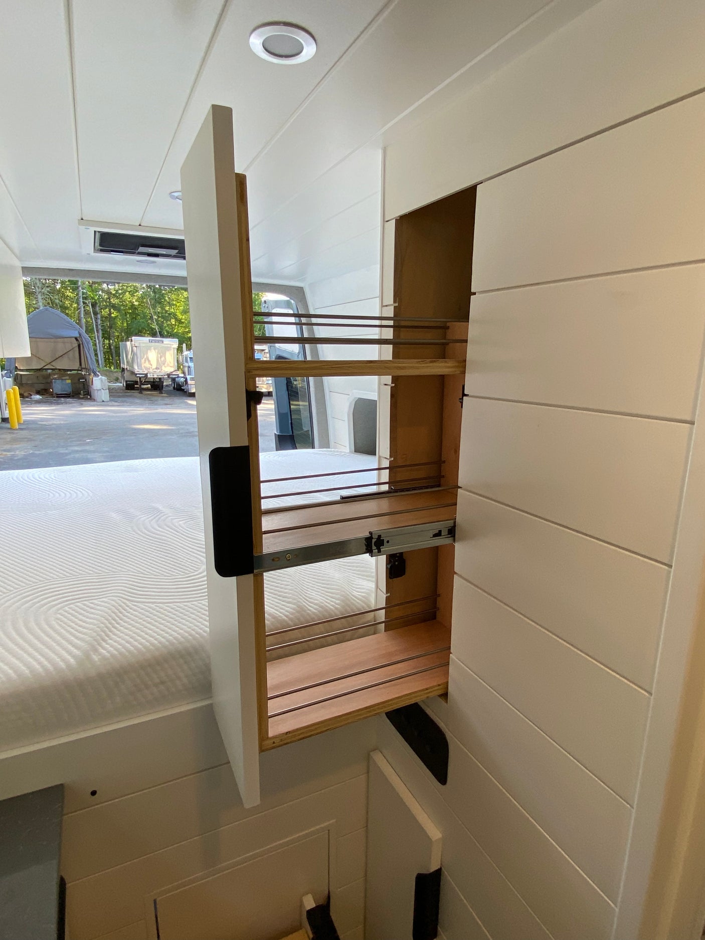 RV rental's smart interior shows a pulled-out pantry storage unit, white shiplap walls, and a comfy bed. Perfect for travel.