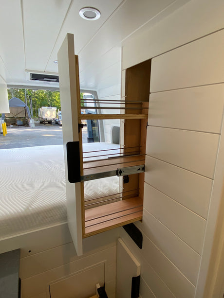 RV rental's smart interior shows a pulled-out pantry storage unit, white shiplap walls, and a comfy bed. Perfect for travel.