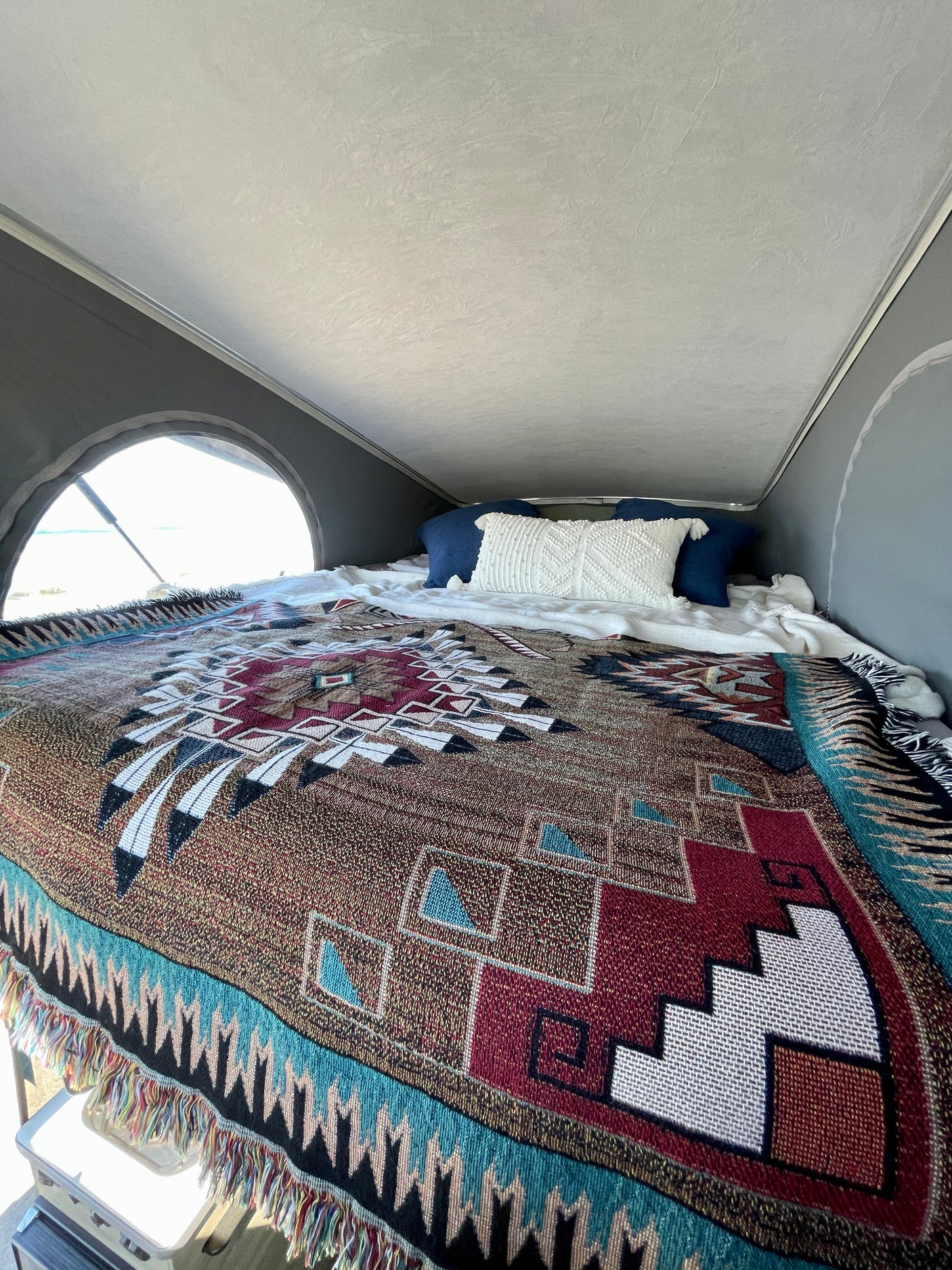 Cozy sleeping area in an RV rental, featuring a vibrant Southwestern blanket and pillows, with a bright window view of the outdoors.