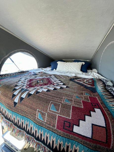 Cozy sleeping area in an RV rental, featuring a vibrant Southwestern blanket and pillows, with a bright window view of the outdoors.