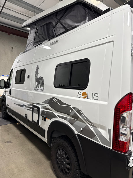 Side view of a white Solis camper van with pop-top roof and mountain graphics, perfect for your next RV rental.