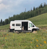 Exploring nature in an RV rental: white camper van parked in a scenic field with wildflowers & a bike.