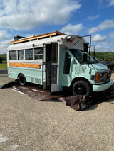 Pastel teal & white skoolie (converted school bus) on asphalt with open door. Unique RV rental for your next adventure!
