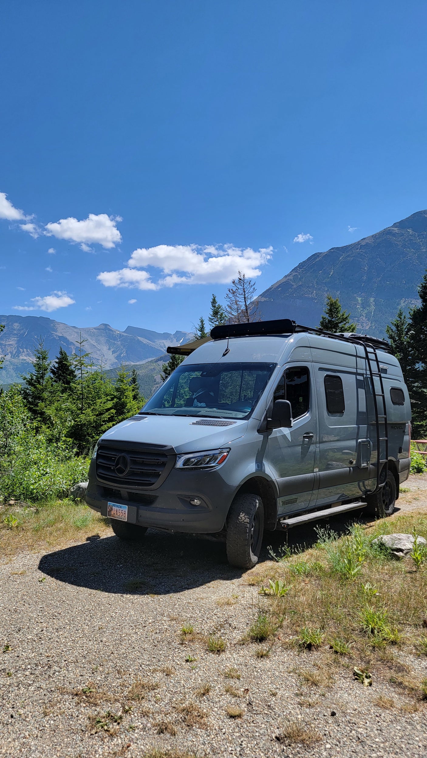 This grey Mercedes-Benz RV rental is parked on a gravel road, offering stunning mountain views for outdoor adventures.