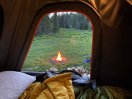Experience tranquil nature from your cozy RV rental! A warm campfire glows in a lush meadow, surrounded by a serene forest.