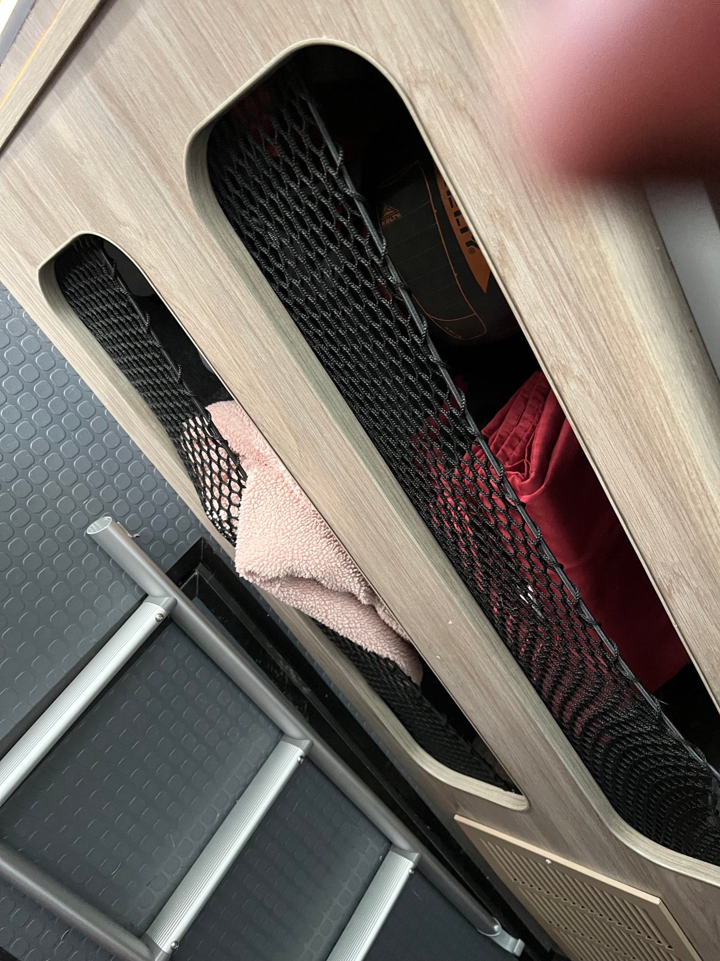 RV rental interior shows wood-paneled walls with mesh storage pockets holding a pink towel & gear. Features floor & ladder.