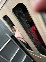 RV rental interior shows wood-paneled walls with mesh storage pockets holding a pink towel & gear. Features floor & ladder.