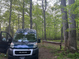 Dave & Matt Vans rv rental: A blue Ram ProMaster van, with a person entering, parked in a green forest for camping.