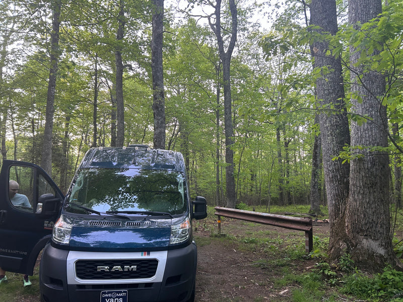 Dave & Matt Vans rv rental: A blue Ram ProMaster van, with a person entering, parked in a green forest for camping. — photo 5