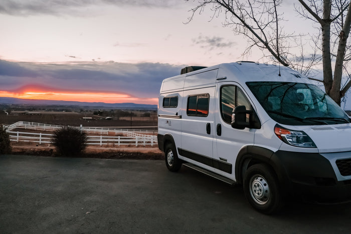 White Winnebago Solis Pocket RV rental at sunset, parked with a vibrant orange sky over a fenced valley.