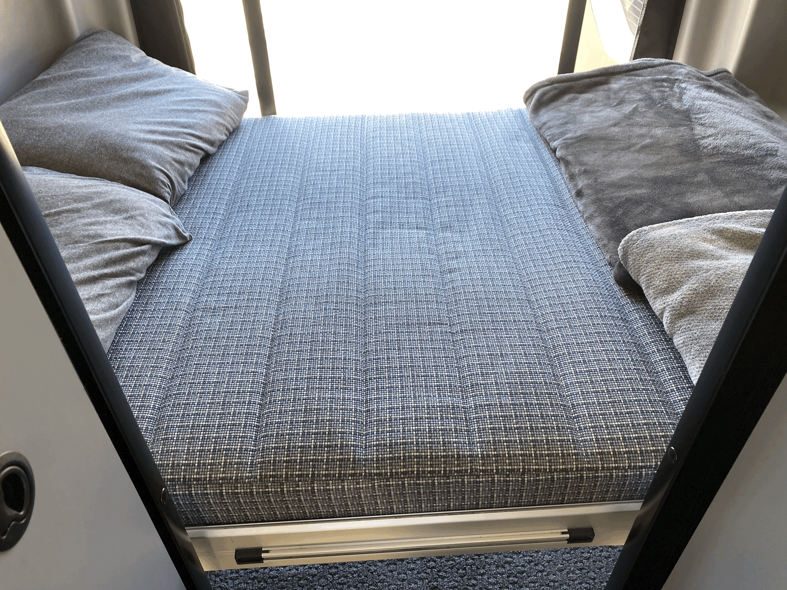 Cozy RV rental sleeping area featuring a patterned mattress, soft pillows, and blankets for comfortable travel.