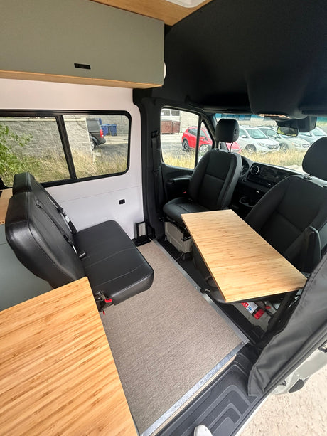 RV rental: Inside a modern camper van conversion, featuring bamboo tables, a rear bench seat, and front cockpit.