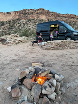 Enjoying an RV rental adventure: Kids, dogs, and a cozy campfire in a desert setting with rocky cliffs.