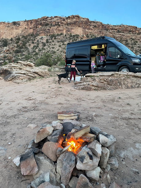 Enjoying an RV rental adventure: Kids, dogs, and a cozy campfire in a desert setting with rocky cliffs.