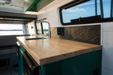 Spacious RV rental interior featuring a modern kitchen with wooden counters, a sink, and a large window view. Ideal for road trips.