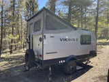 A modern Viking pop-up RV rental is perfectly nestled in a sunny, pine forest clearing, ready for your next outdoor adventure.